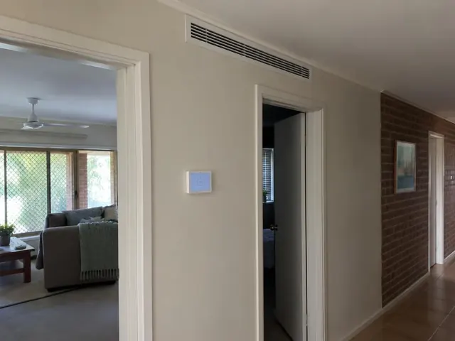 Ceiling return-air grille and wall controller in a hallway beside brick feature walls in Paradise Point